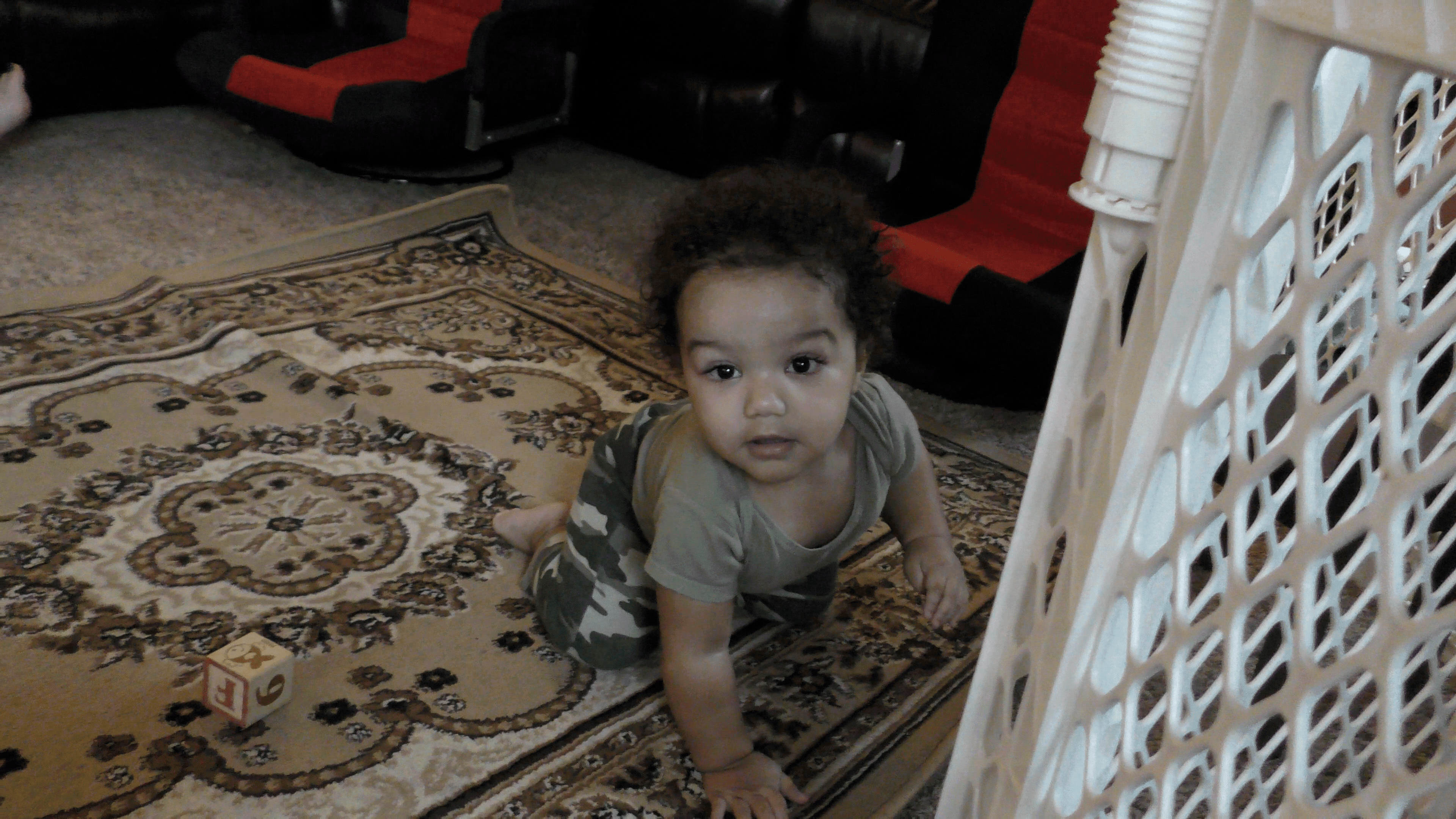 Toddler boy looking ahead from a crawling position on a living room floor.