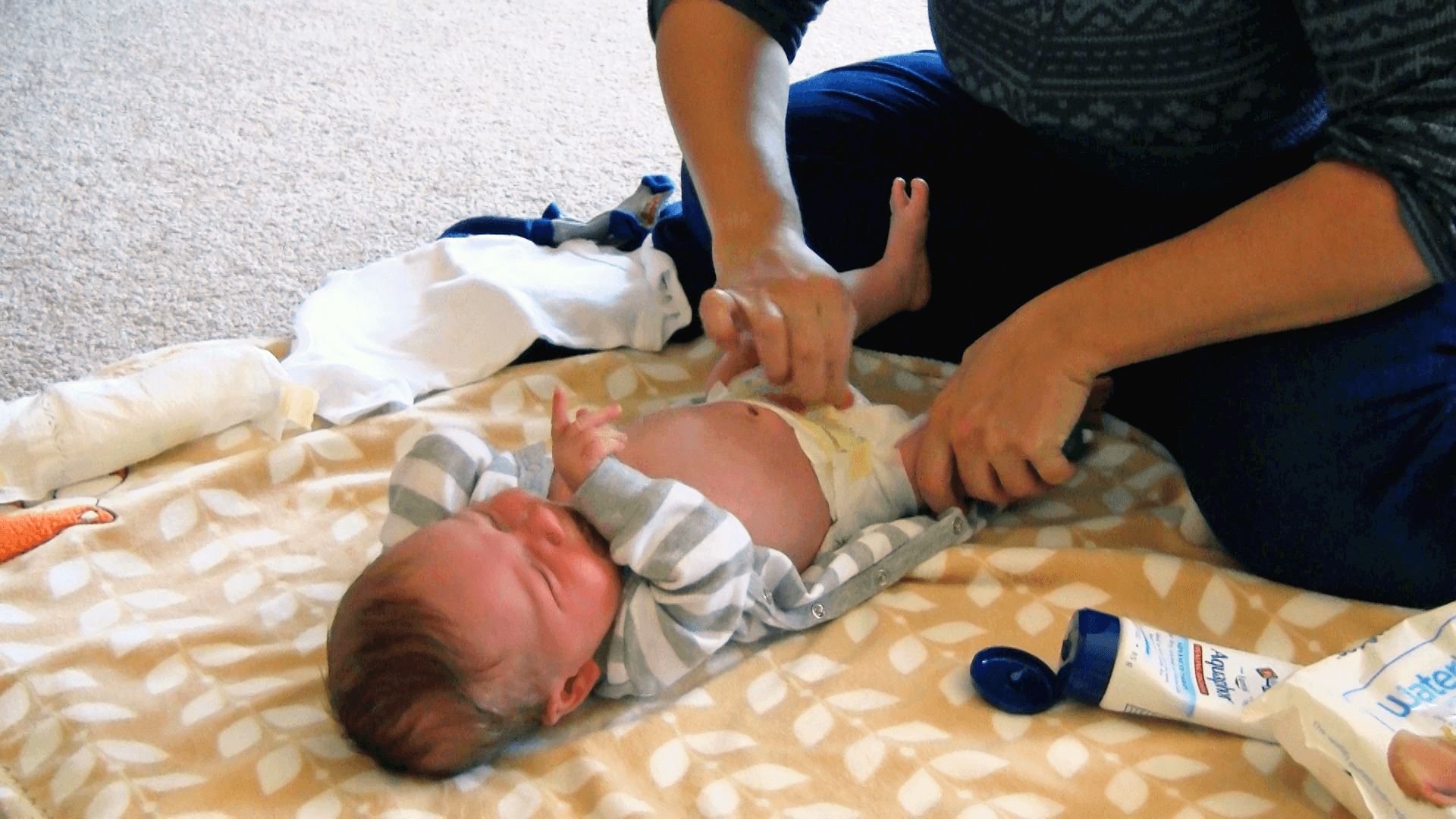 Baby getting their diaper changed on a blanket on the floor surrounded by diaper changing items.
