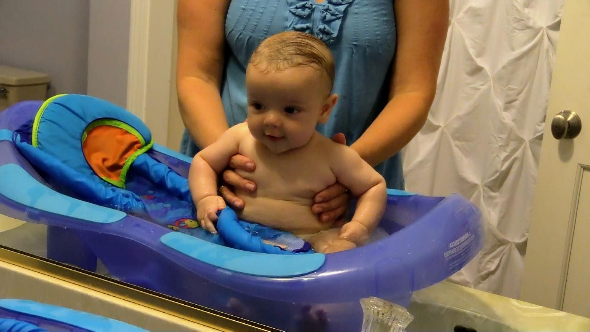 Mom sitting baby upright in baby tub on bathroom counter and looking into the mirror together.