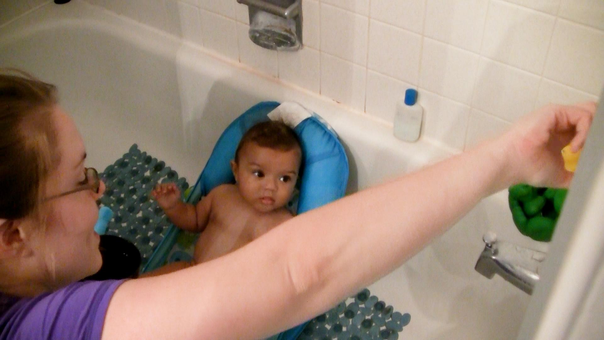 Mom playing with baby boy in the bathtub by pointing out toys on bathtub wall.