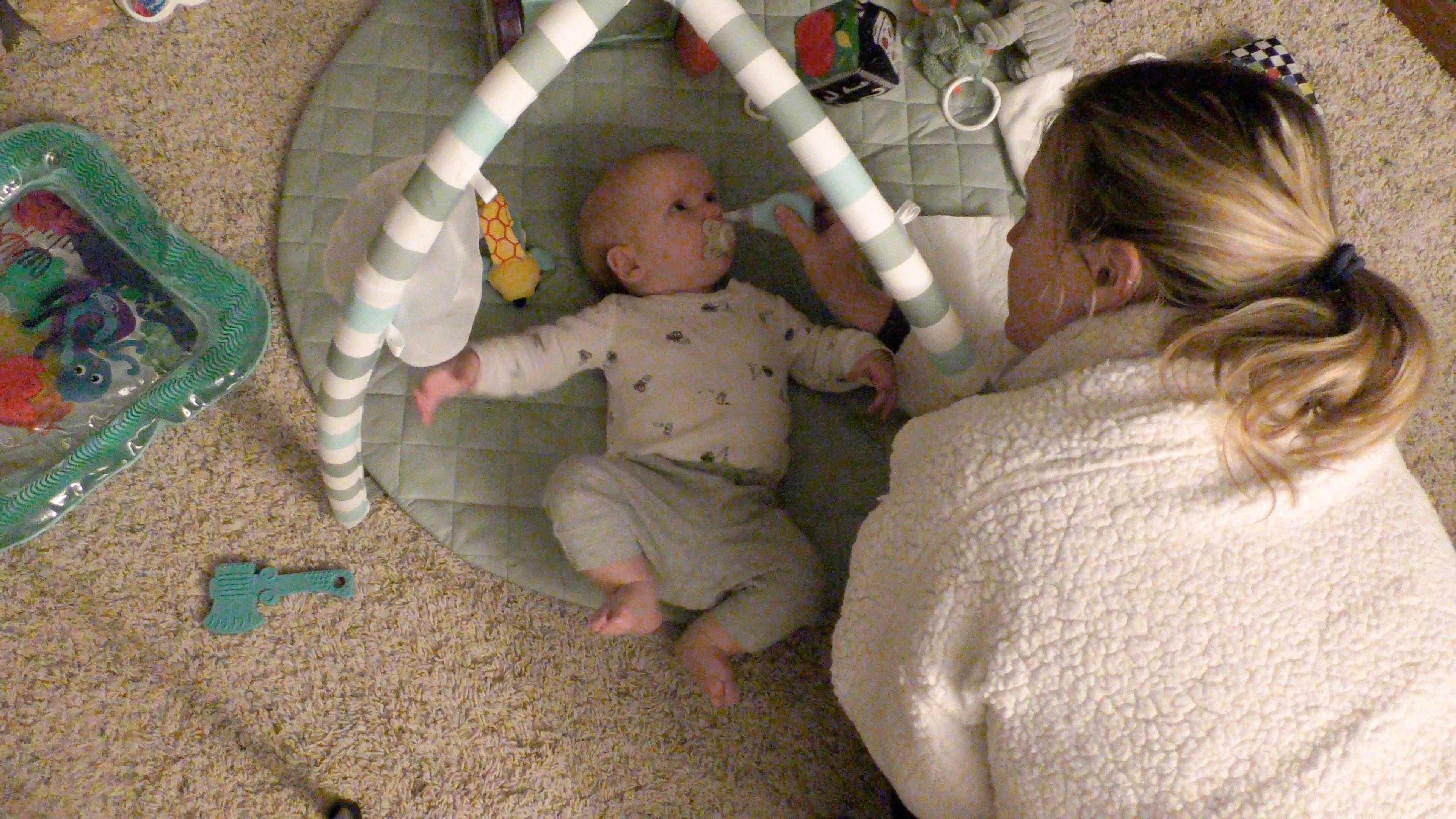 Mom using a bulb syringe to clean baby boy’s nose while he lies on back underneath a baby mobile play mat.