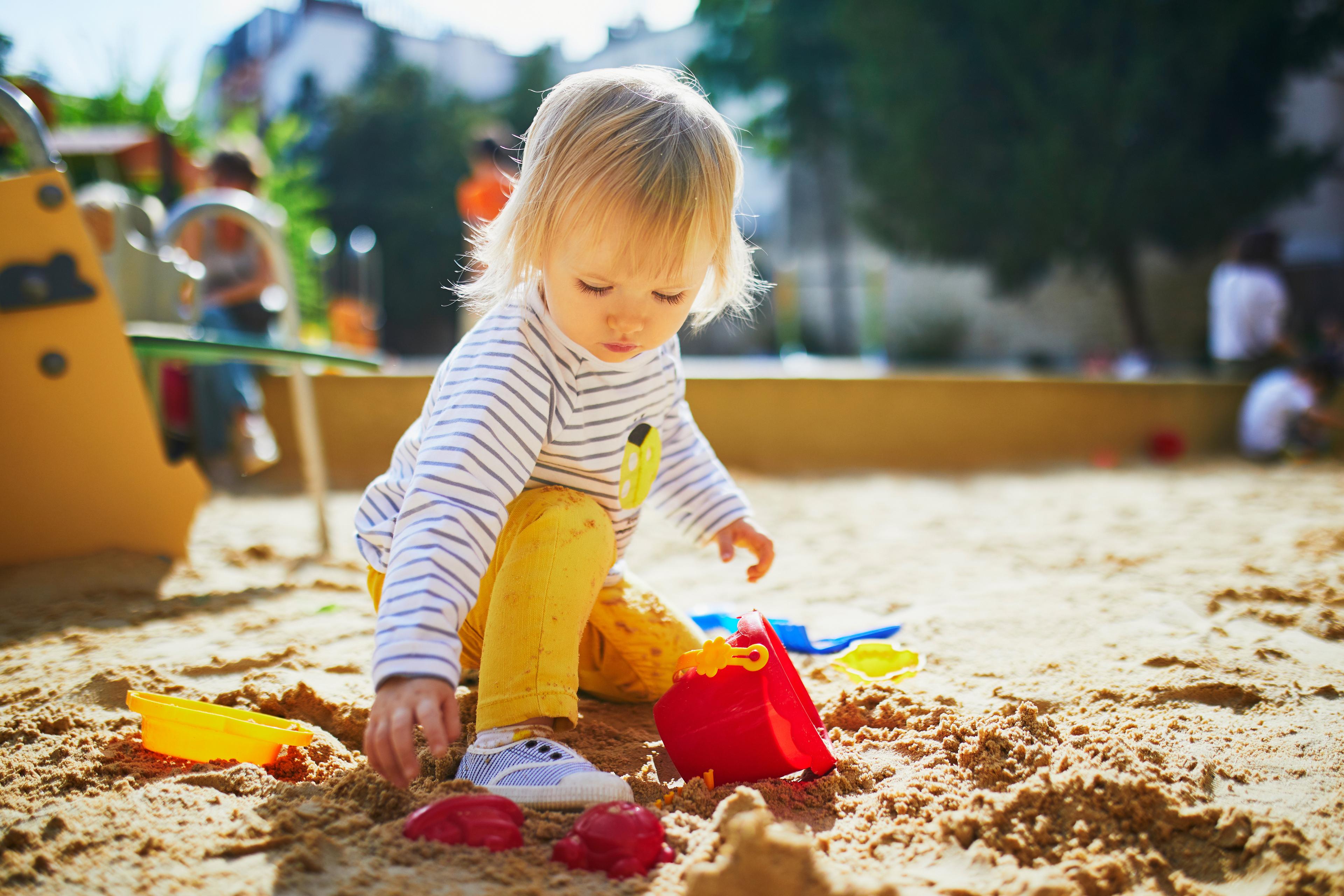 Young girl playing independently in a sandpit at the playground.