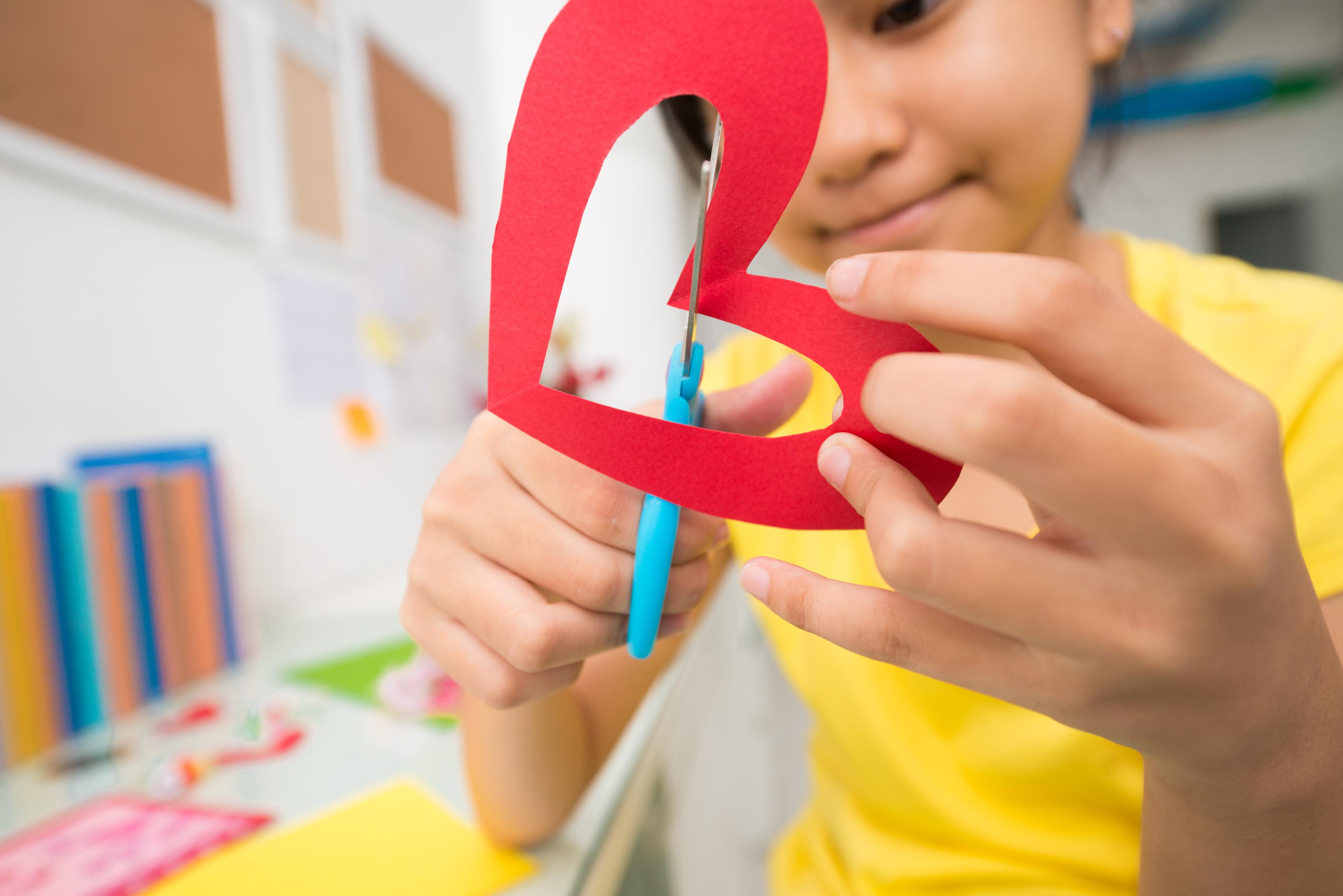 Child using blue safety scissors to cut a red paper heart during a craft activity.