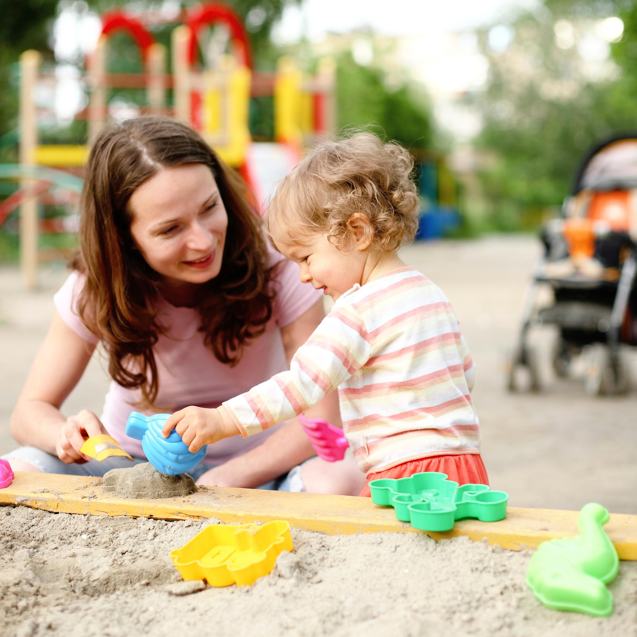 Mom and daughter using sand toys to play in a sandbox at a playground.