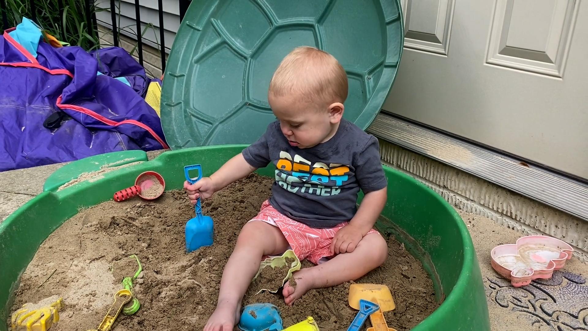  Toddler boy digging up sand with a toy shovel for his pretend construction site.