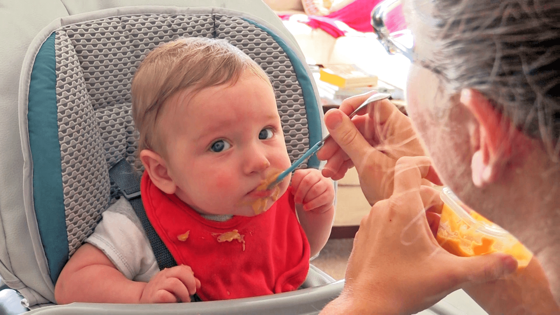 Baby boy being spoon-fed orange puree while sitting in a high chair.