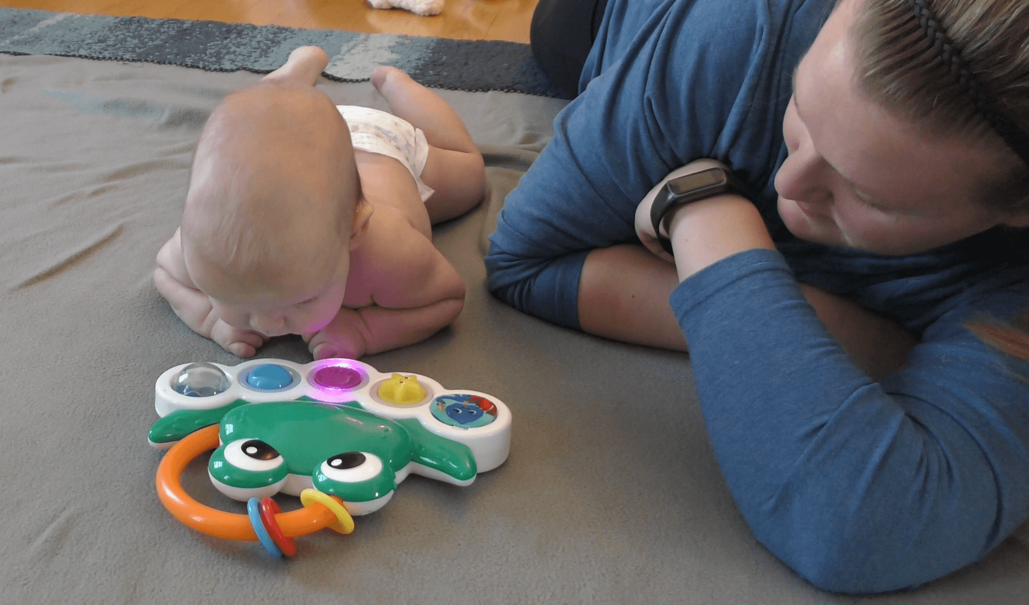 Newborn boy and mom lying on their tummies side by side and playing with a light-up toy.