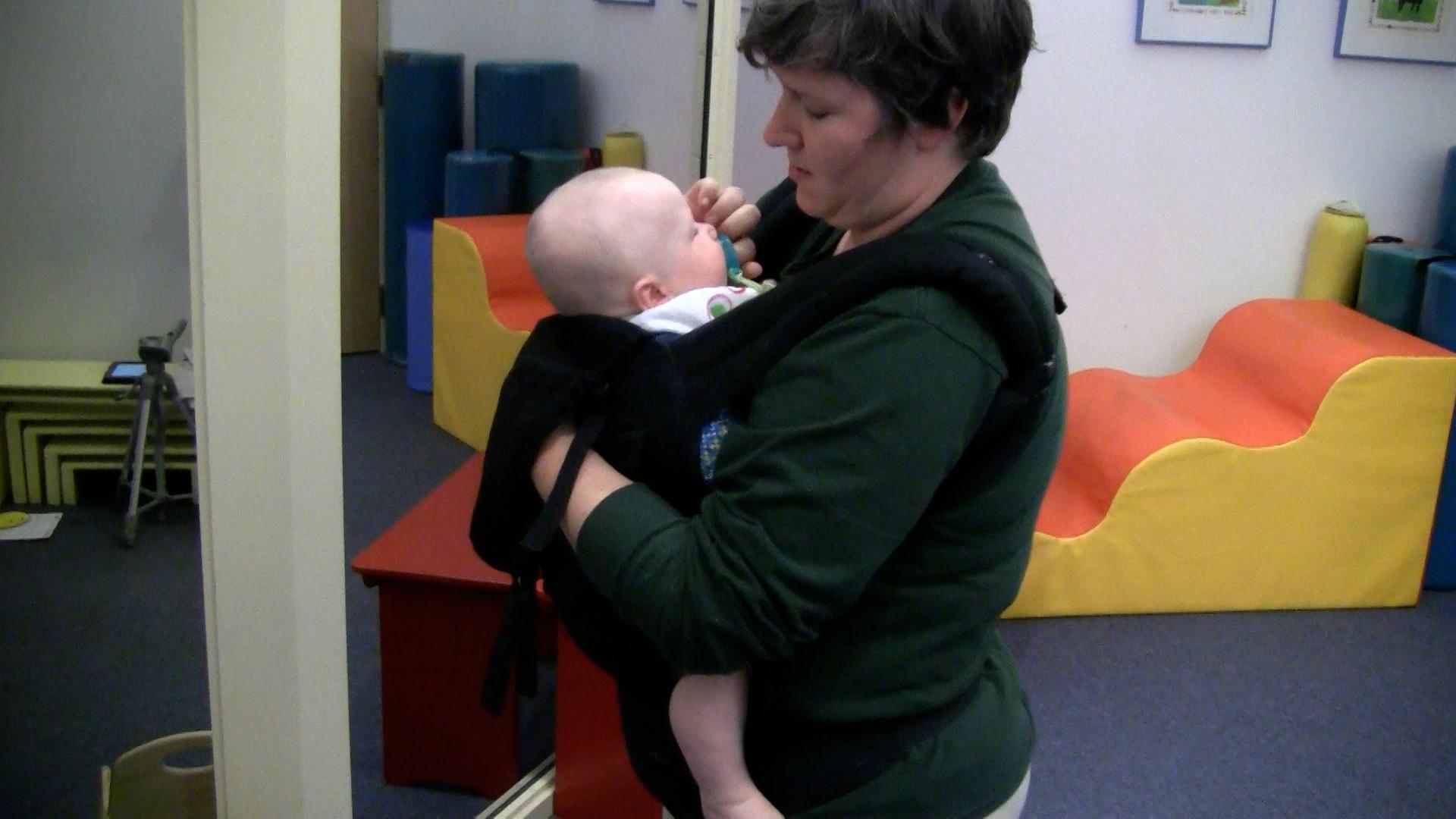 Parent using soft-structured baby carrier to babywear around play room.