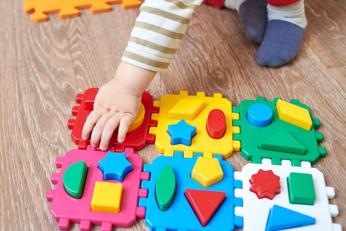 Close-up of a baby learning shapes through a colorful puzzle mat, practicing early math skills like shape and color recognition.