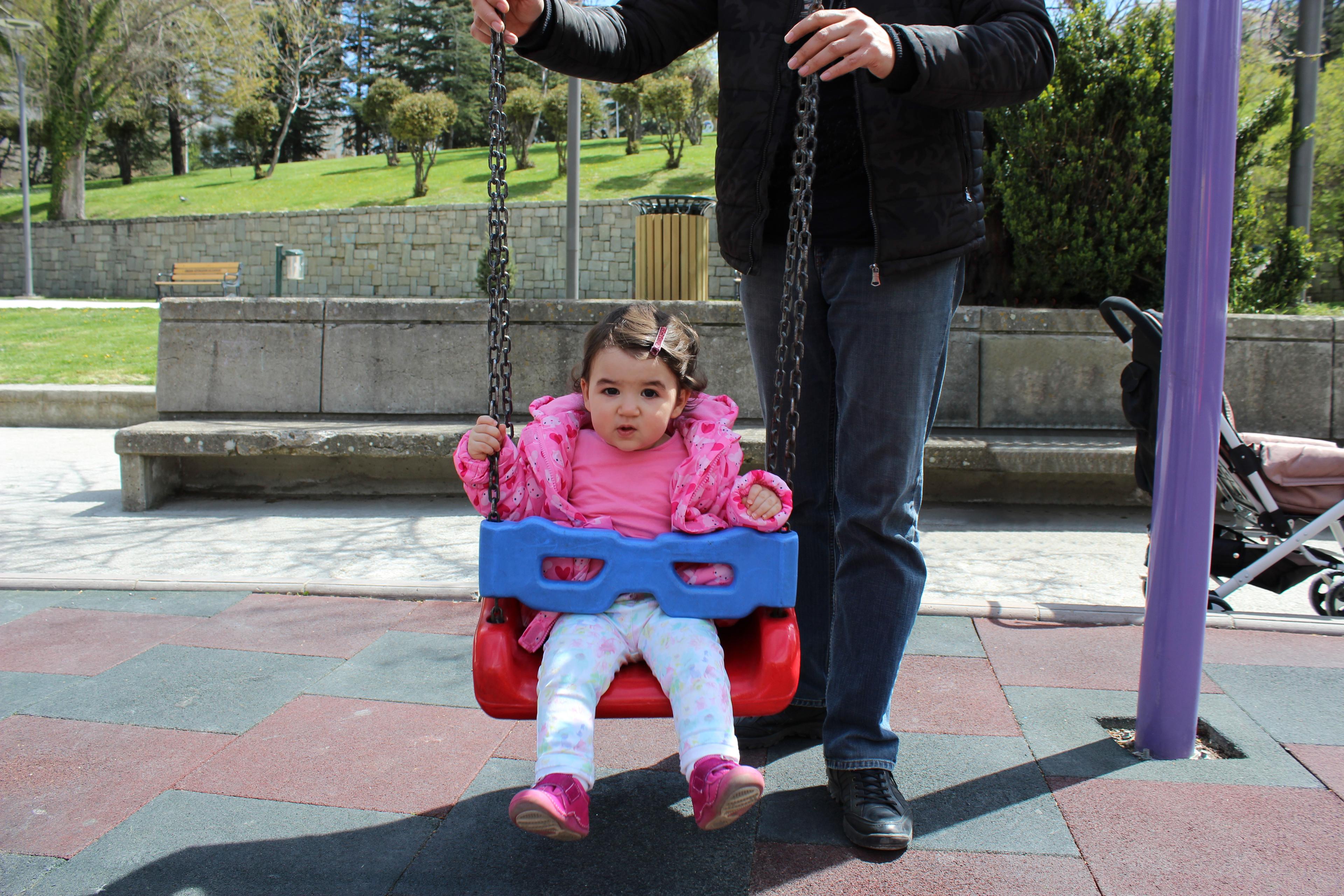 Dad pushing baby girl in an outdoor swing to build balance, body awareness, and core strength.