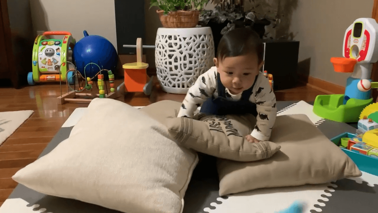 Baby boy crawling over a pile of pillows, an example of risky play at this age.