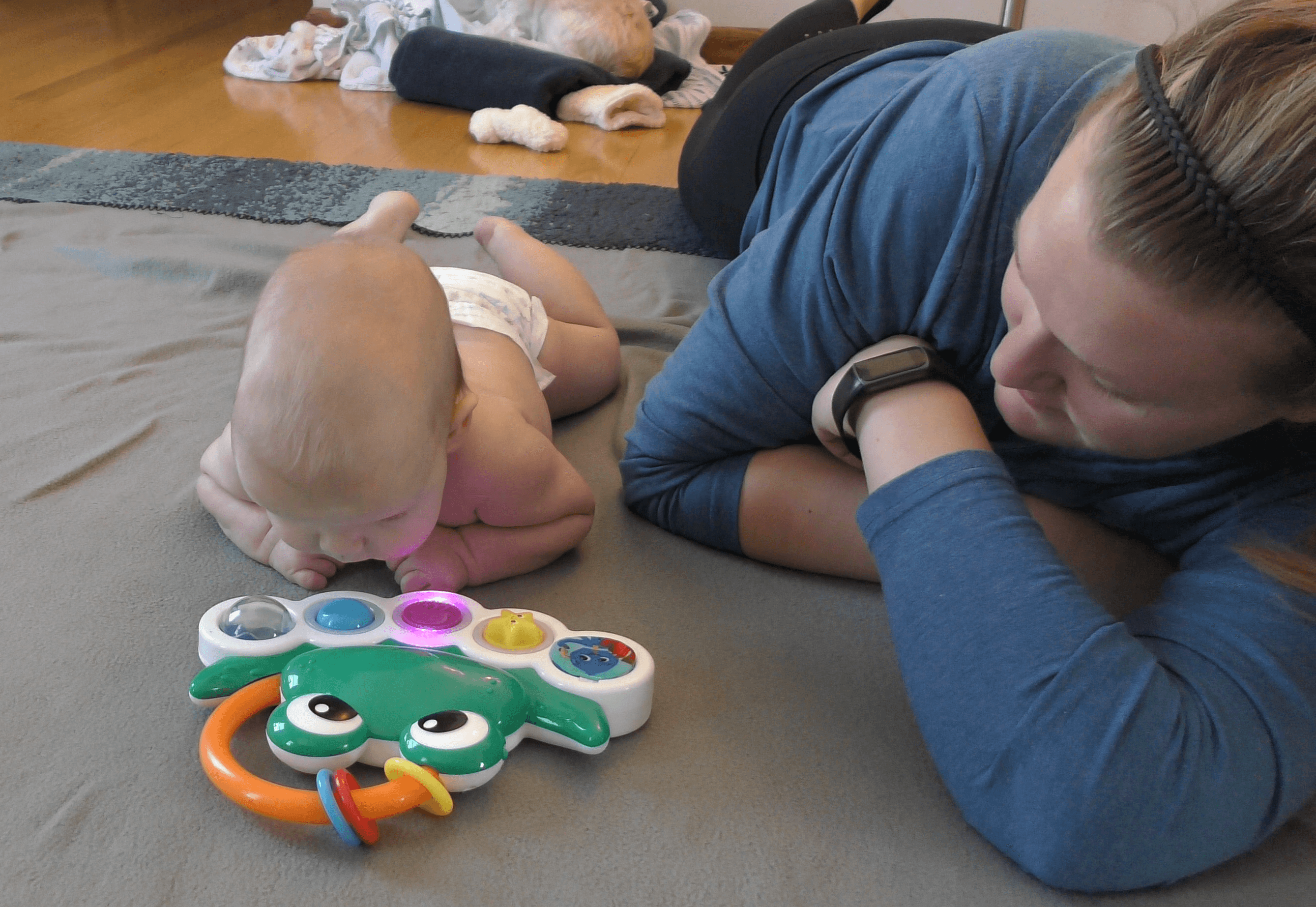 Baby boy lifting head up to look at musical, light-up frog toy while on his tummy alongside mom.