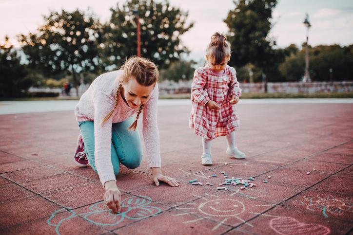Mother and child drawing with sidewalk chalk outdoors to practice fine motor and communication skills.