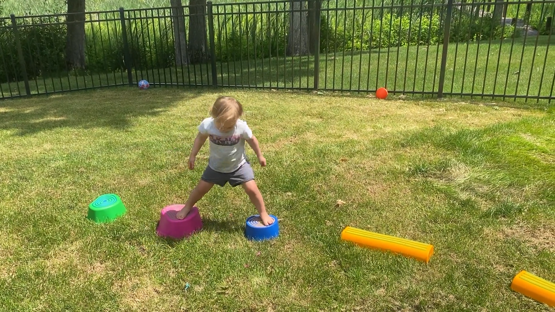 Toddler girl balancing between two stepping stones in a backyard obstacle course.