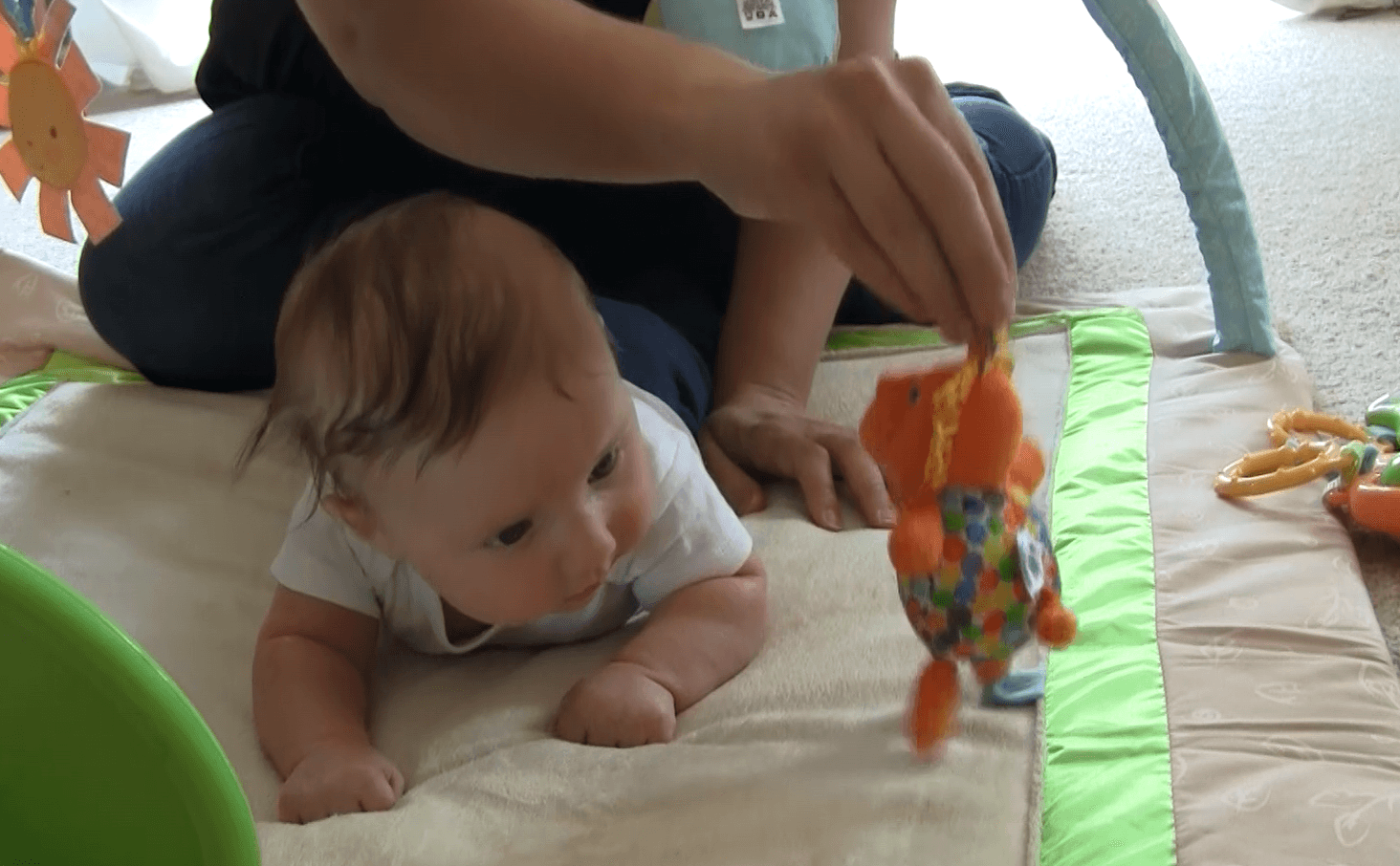 Baby boy lying tummy-down playmat while holding head his up to look at stuffed animal mom is dangling in front of him.